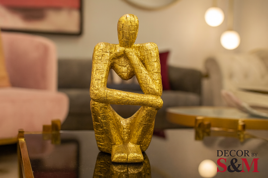 Golden thinking figure sculpture on glass table in contemporary living space