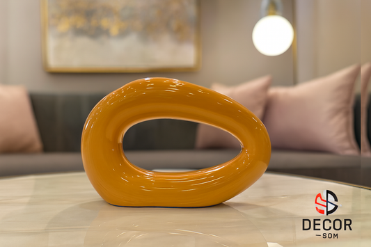 Orange ceramic sculpture with horizontal opening on glass table in contemporary living space